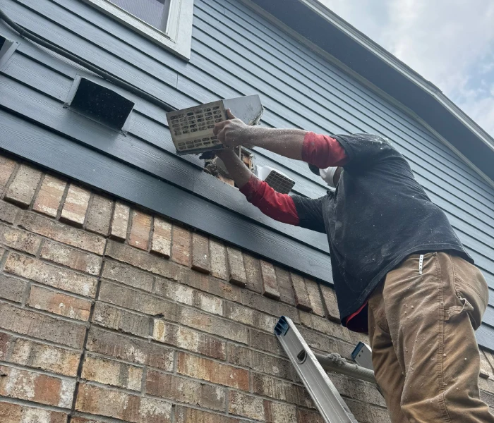 Supreme Air Care technician cleaning a clogged exterior dryer vent at a residential home in Austin, TX.