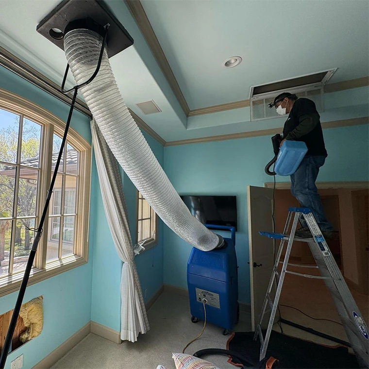 Technician cleaning ceiling air ducts with commercial-grade negative air equipment
